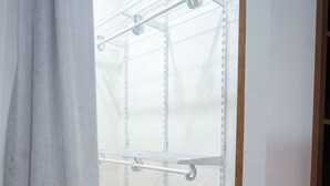 Un vestidor con estanterías metálicas, una cortina gris y suelo de madera.