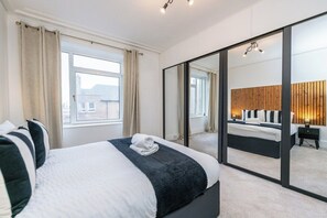 Ein modernes Schlafzimmer mit einem großen Bett, einem Spiegel und Blick auf einen anderen Raum.