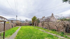 A residential backyard with a stone wall, a grassy lawn, and a pathway. - The Blue Toon Retreat | 3 Bed Apartment (Aberdeenshire)