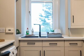 A kitchen with a window, a sink, cabinets, and a countertop with a dish rack and a bottle.
