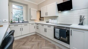 A modern kitchen with white cabinetry, a built-in oven, a microwave, and a window providing natural light. - The Blue Toon Retreat | 3 Bed Apartment (Aberdeenshire)