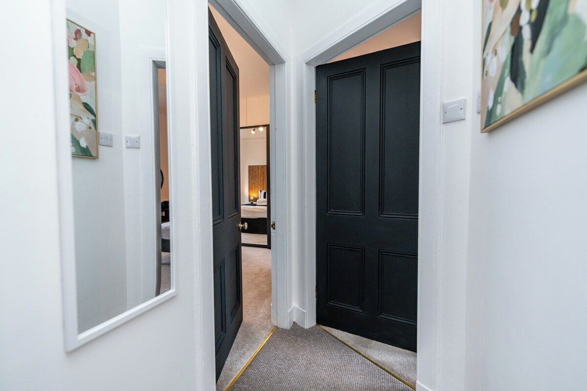A hallway with a dark door, a light-colored wall, and a carpeted floor.