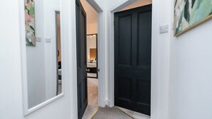A hallway with a dark door, a light-colored wall, and a carpeted floor. - The Blue Toon Retreat | 3 Bed Apartment (Aberdeenshire)