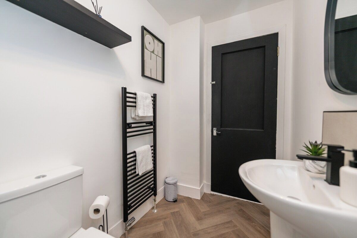 A bathroom with a white sink, black towel rack, a black door, and a white toilet.