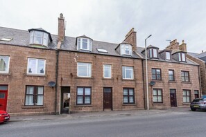 A row of terraced houses with multiple windows, a red door, and a parked car. - The Blue Toon Retreat | 3 Bed Apartment (Aberdeenshire)
