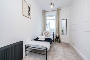 A bedroom with a bed, radiator, window, curtains, and a hanging light fixture. - The Blue Toon Retreat | 3 Bed Apartment (Aberdeenshire)