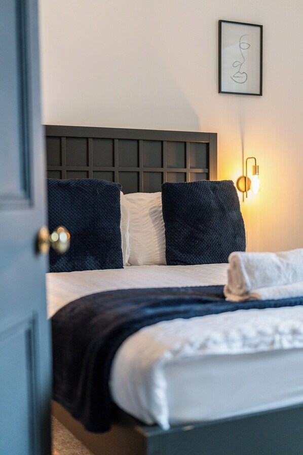 A hotel room with a bed, a headboard, a wall-mounted light, and a framed picture.