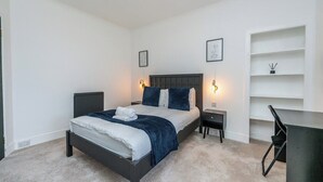 A bedroom with a bed, bedside tables, a desk, and shelving. - The Blue Toon Retreat | 3 Bed Apartment (Aberdeenshire)