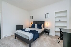 A bedroom with a bed, bedside tables, a desk, and shelving.