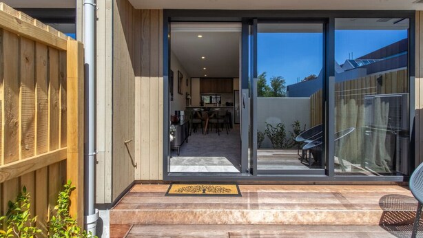 Una casa moderna con un portón corredizo de vidrio que da a un patio con comedor y un coche estacionado afuera.