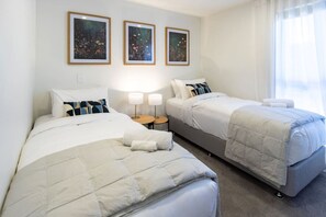 A hotel room with two beds, a small table with lamps, and three framed floral artworks on the wall. - Peaceful City Townhouse | 2 Bed+ Private Car Park (Christchurch)
