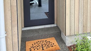 Entrada de un edificio moderno con una puerta oscura, felpudo con diseño de árbol y pared de paneles de madera.