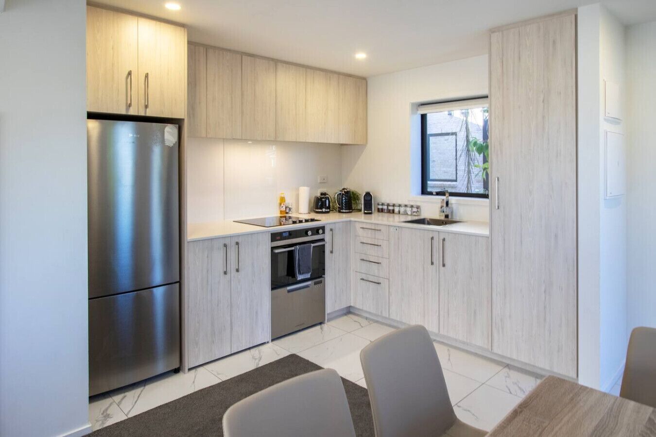 Una cocina moderna con electrodomésticos de acero inoxidable, armarios de madera clara y un ventanal que proporciona luz natural.