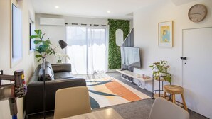 Una sala moderna con sofá, televisor, escalera y una pared cubierta de plantas.