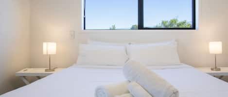 A hotel room with a large bed, two bedside lamps, and a window with a view of trees.
