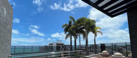 A rooftop terrace with a pool, palm trees, and a view of the ocean.