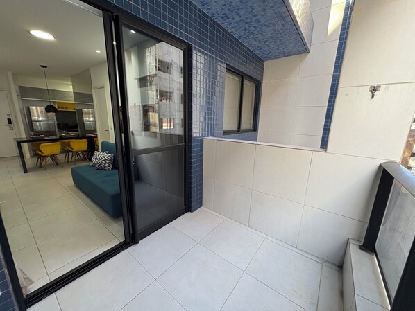 Interior moderno com porta de correr de vidro que dá para uma sala de jantar, um sofá e uma cozinha ao fundo.