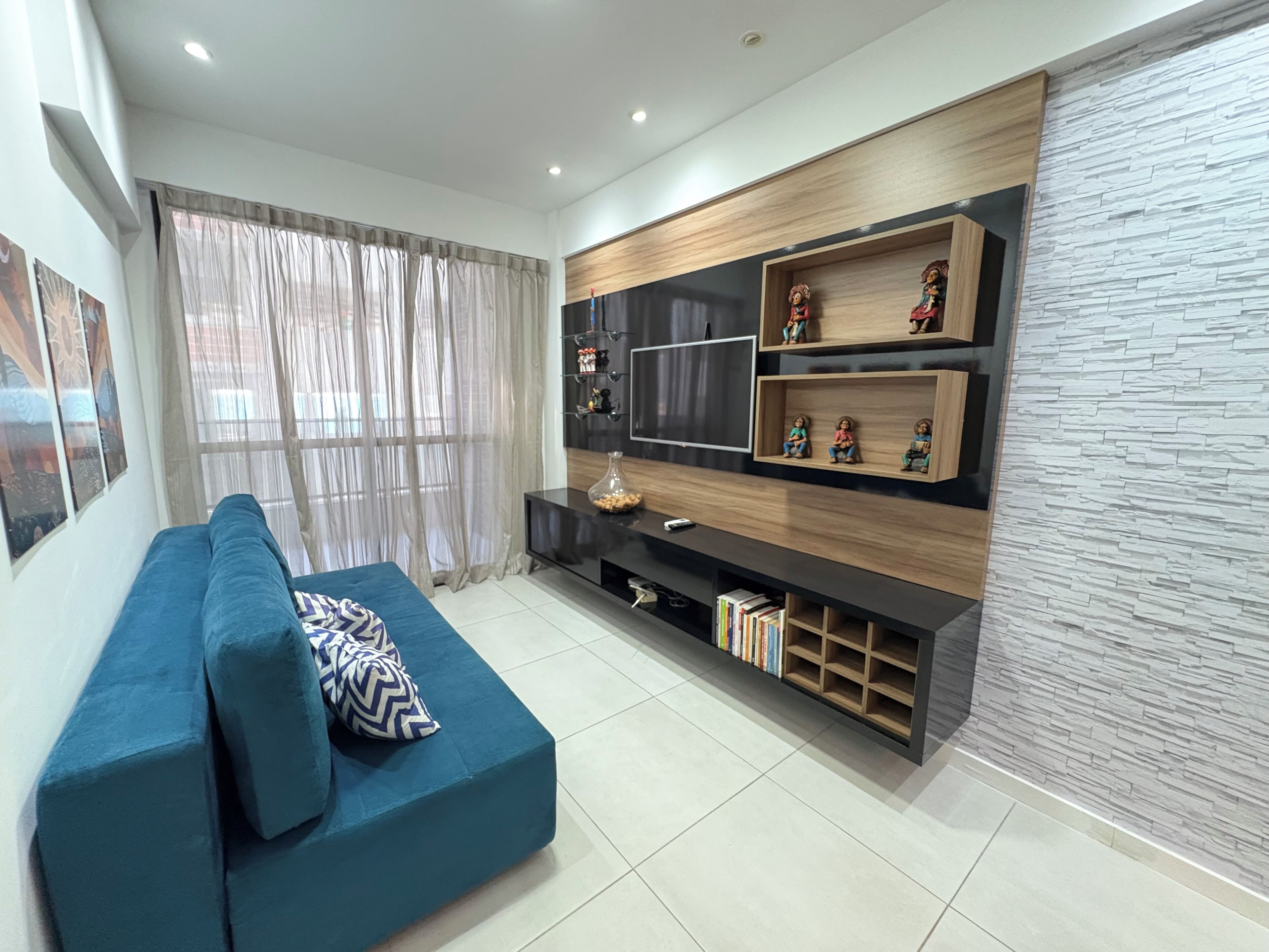 A modern living room with a blue sofa, a TV stand with shelves, and a stone-textured wall.