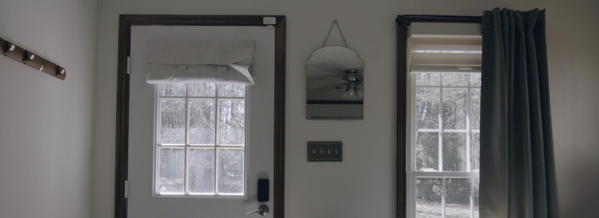 Une pièce avec une porte, une fenêtre donnant sur des arbres, un luminaire fixé au mur et une prise de courant.