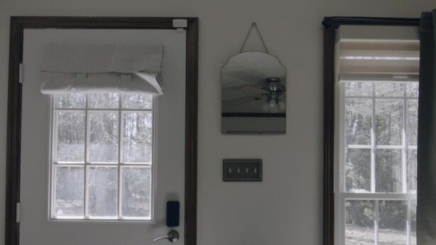 Une pièce avec une porte, une fenêtre donnant sur des arbres, un luminaire fixé au mur et une prise de courant.