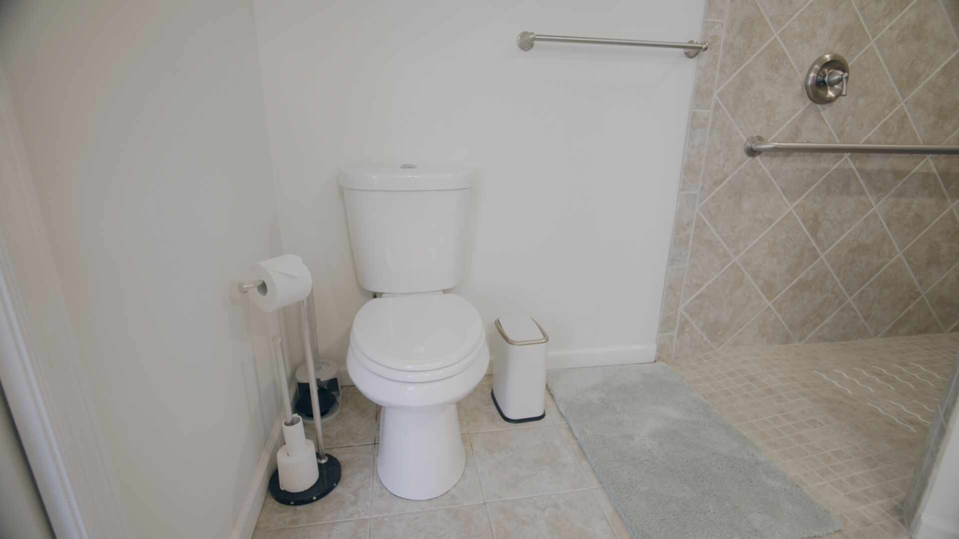 A bathroom with a toilet, a hand dryer, a trash bin, and a shower area.