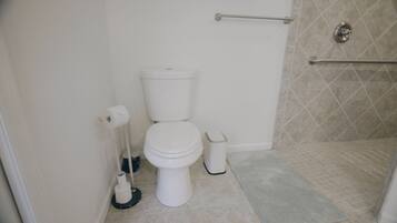 A bathroom with a toilet, a hand dryer, a trash bin, and a shower area.