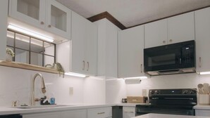 A modern kitchen with white cabinets, a stainless steel range hood, and a built-in microwave. - Luxurious 1-Bedroom Townhome in Peachtree City with AC (Peachtree City)