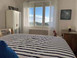 A bedroom with a bed, a radiator, a window with curtains, a wardrobe, and a framed picture on the wall. - Crozon soleil ! (Crozon)