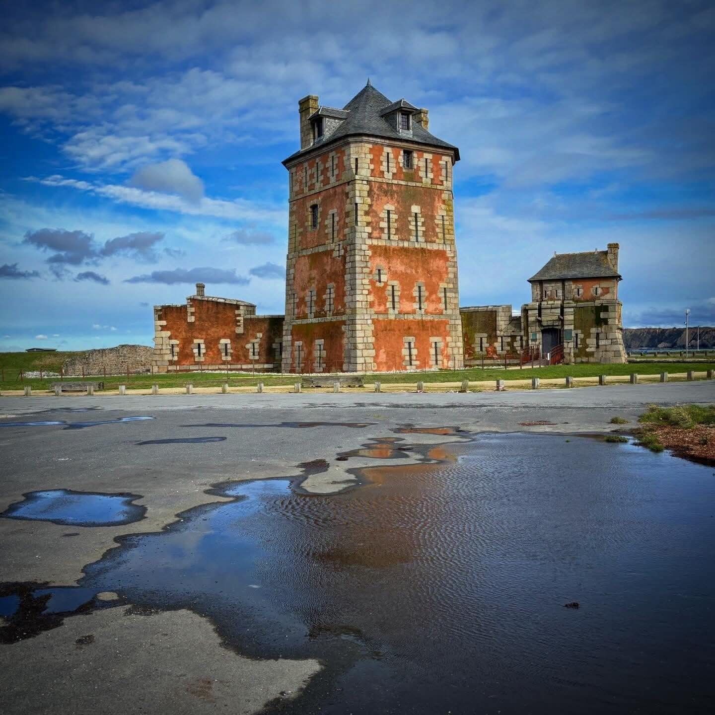 A historic building with a prominent tower, a courtyard with puddles, and a clear sky.