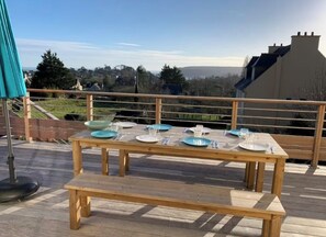 A wooden deck with a table set for a meal, overlooking a residential area. - Crozon soleil ! (Crozon)