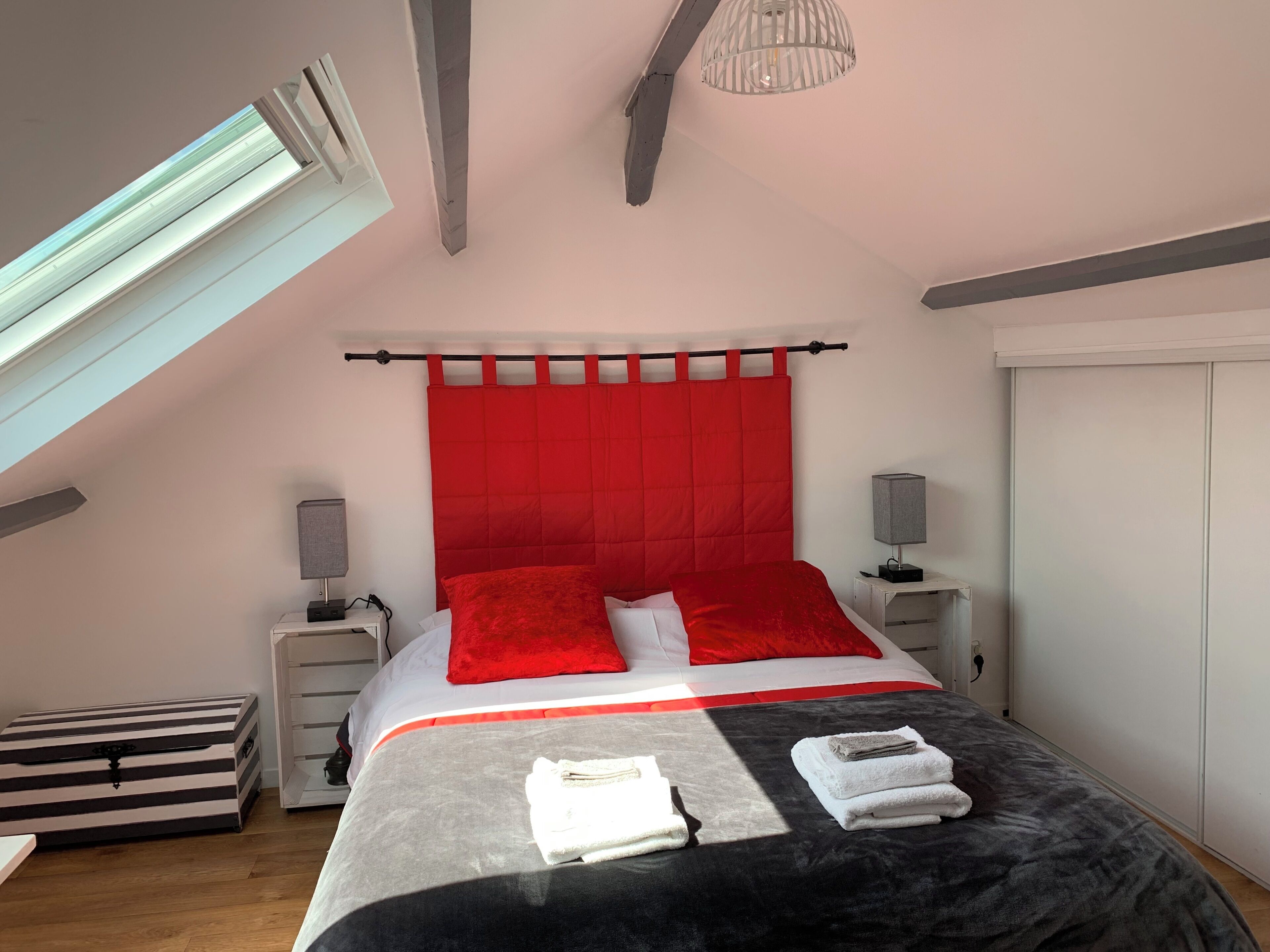 Une chambre à coucher avec un lit, une tête de lit rouge, des lampes de chevet, un meuble de rangement à rayures et une armoire.