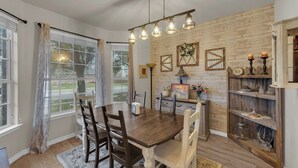 Ein Essbereich mit Holztisch, Stühlen, einer Chandelüster und einer rustikalen Wand mit Dekorationen.