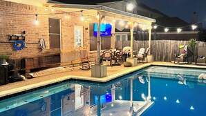 Ein Swimmingpool mit überdachtem Patio, Sitzgelegenheiten im Freien und einer Ziegelwand.