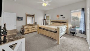 Ein Schlafzimmer mit Bett, Schreibtisch, Stuhl, Kommode, Spiegel und Deckenventilator.