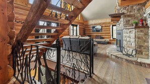 Ein Blockhaus-Interieur mit Kamin aus Stein, einer Holztreppe und einer gemütlichen Wohnbereitschaft.