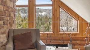 Ein Zimmer mit Steinwand, Fenster mit Blick auf einen Wald und ein Sessel mit Kissen.