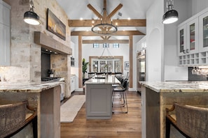 A kitchen with a central island, wooden beams, pendant lighting, and a dining area with chairs and a table. - Lost Creek Lodge - 2 blocks from Main with Pool (Fredericksburg)