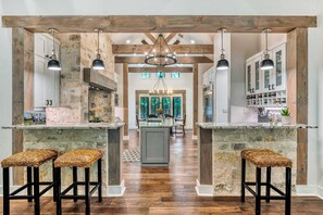 A kitchen with stone walls, wooden beams, and a central island with stools. - Lost Creek Lodge - 2 blocks from Main with Pool (Fredericksburg)