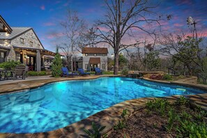 Une piscine avec des chaises longues, un bâtiment en pierre et un ciel dégagé.