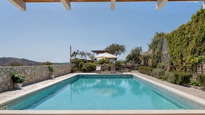 Ein rechteckiger Pool mit einer Steinsäule an einer Seite und einer Holzpergola darüber.