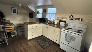 Une cuisine avec des meubles blancs, une cuisinière et un coin repas comprenant une table et des chaises.
