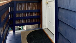 A wooden deck with a metal railing, a glass door with a number '965' sign, and a doormat.