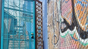 Une porte métallique bleue avec un panneau d’avertissement, une clôture en treillis métallique et un mur couvert de graffitis.