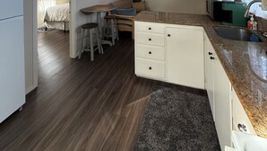 A compact kitchen with a dining area, wooden flooring, and a view into a bedroom.