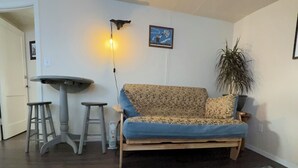 Un salon comprenant un canapé, une petite table, deux tabourets, un tapis, une lampe fixée au mur et une plante en pot.