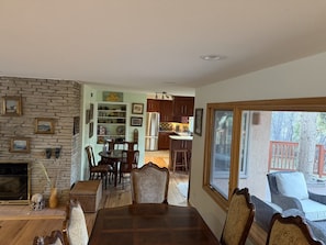 A dining area with a fireplace, wooden dining table, and chairs, leading to a kitchen with wooden cabinets and a refrigerator. - Charming Mountain house in Colorado Springs perfect for your getaway (Colorado Springs)