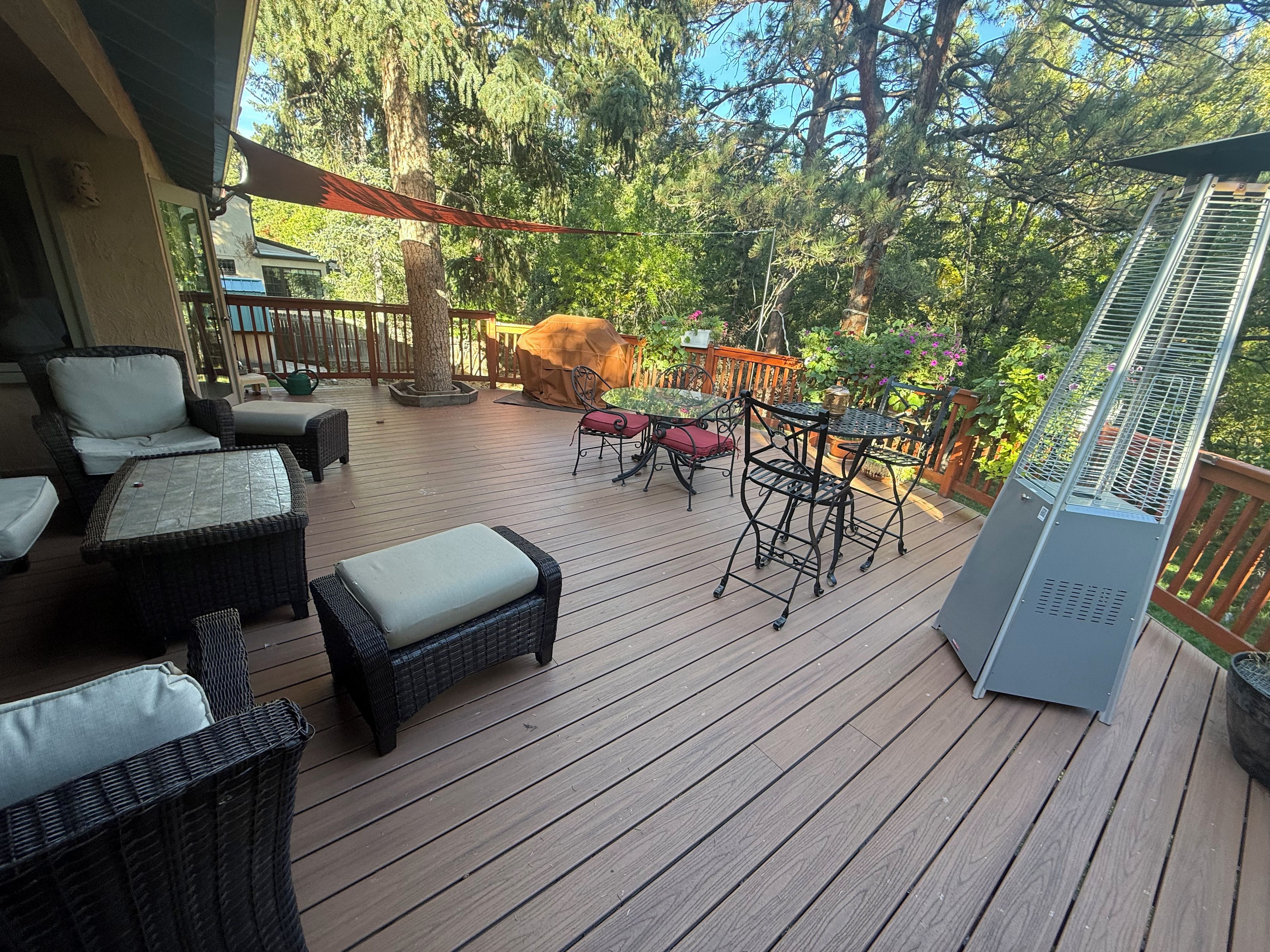 A wooden deck with outdoor furniture, including wicker chairs and a table, surrounded by trees.