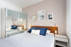 Ein modernes Schlafzimmer mit einem großen Bett, Nachttischen, einem Spiegel und Kunstwerken an der Wand.