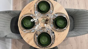 Uma mesa redonda de madeira com pratos verdes e talheres, rodeada por cadeiras estofadas em cinza.