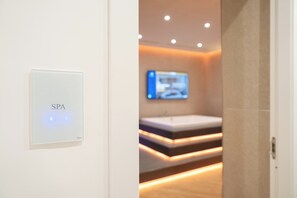 A spa area with a digital sign, a television, and a modern bathroom with a bench. - Napolitano Rooms - FLEGREA spa (Pozzuoli)